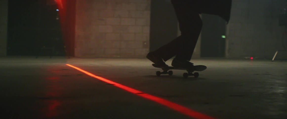 Silhouette of a man over a skateboard inside a room with a red laser line on the floor