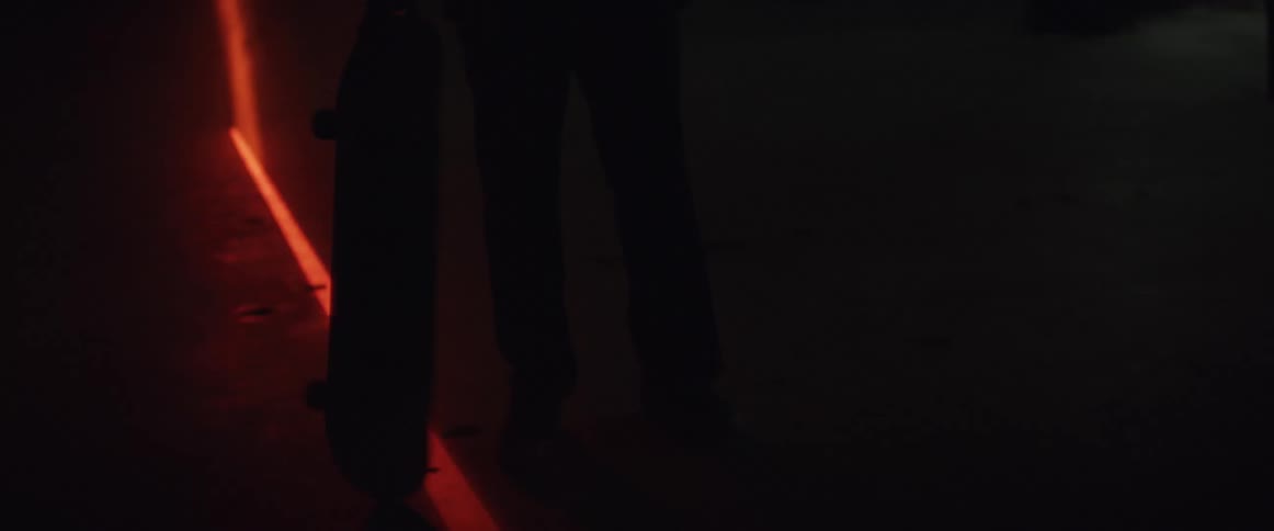 Man spins skateboard on red laser line while standing outdoors at night