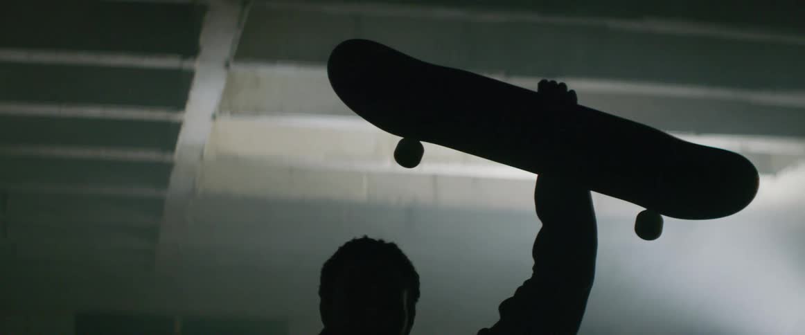 A man is standing inside a structure holding a skateboard in the air above his head
