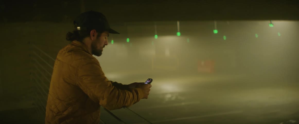 Man stands against rail overlooking foggy parking area and uses his mobile phone