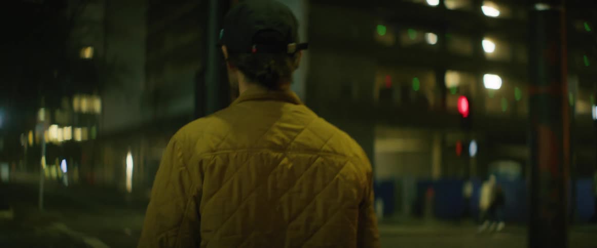 A man walks down a city sidewalk across from two women at night