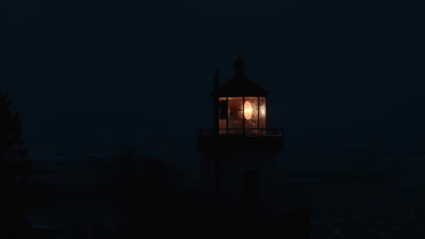 A lighthouse lamp spins and flashes at night