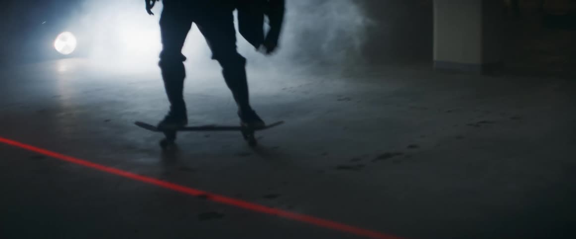 Skateboarder perform jump trick before crossing red laser in foggy area lit by spotlight