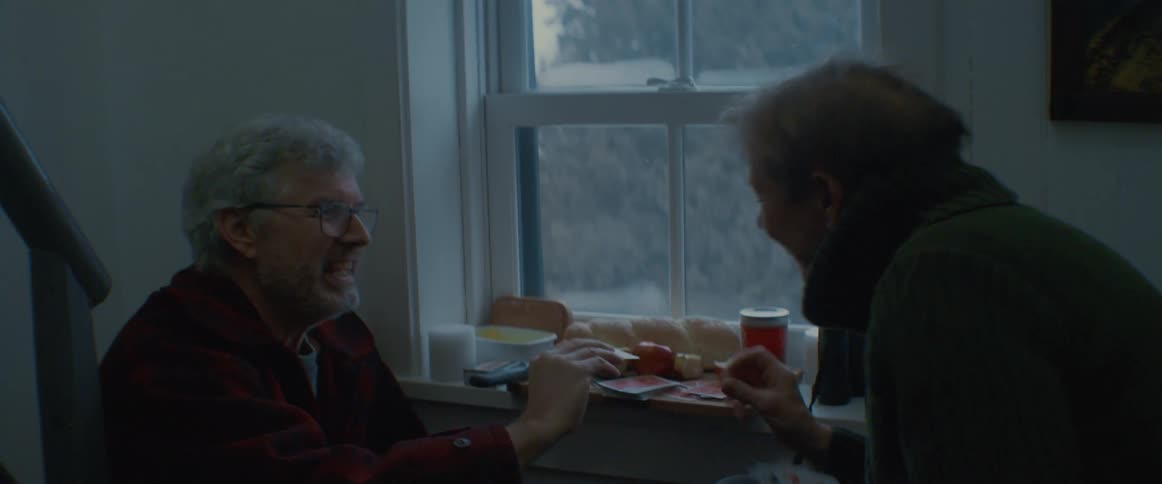 Couple sits near window with cheese tray and play cards