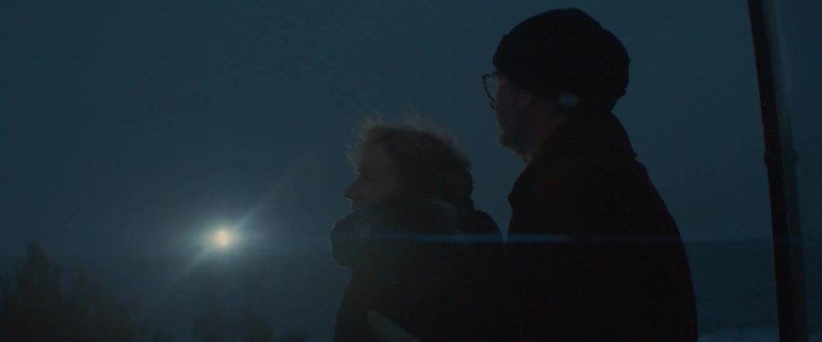 Man hugs woman as they stand outdoors bundled in winter clothes