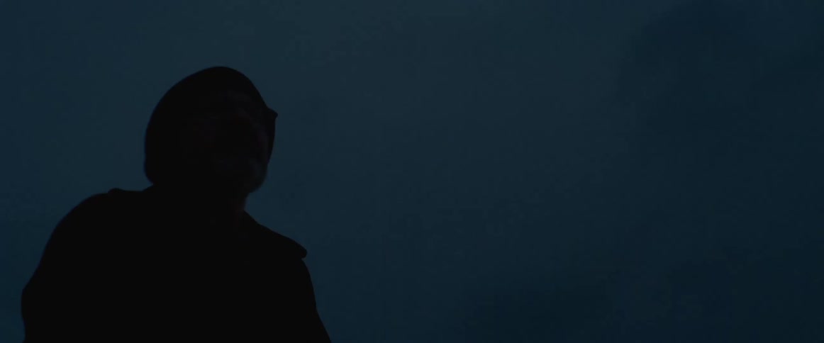 A man wearing glasses is outside on a balcony at night looking up at the sky