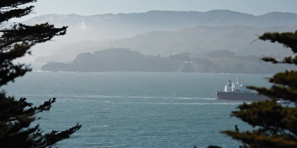 A boat sails across the water through the mist and there are mountains in the distance