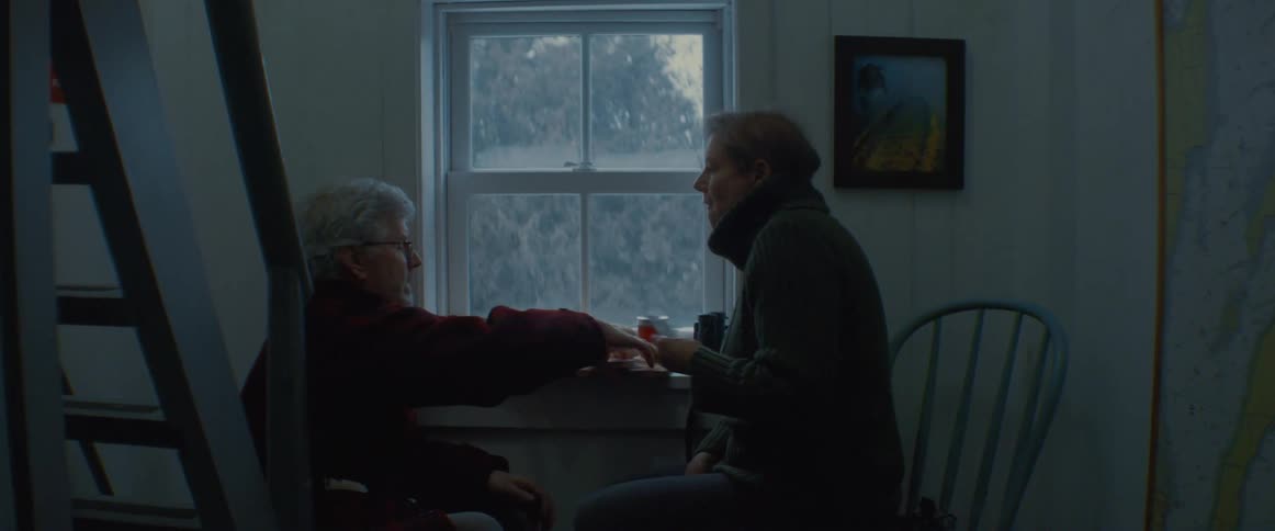 A couple play cards at home in front of a window