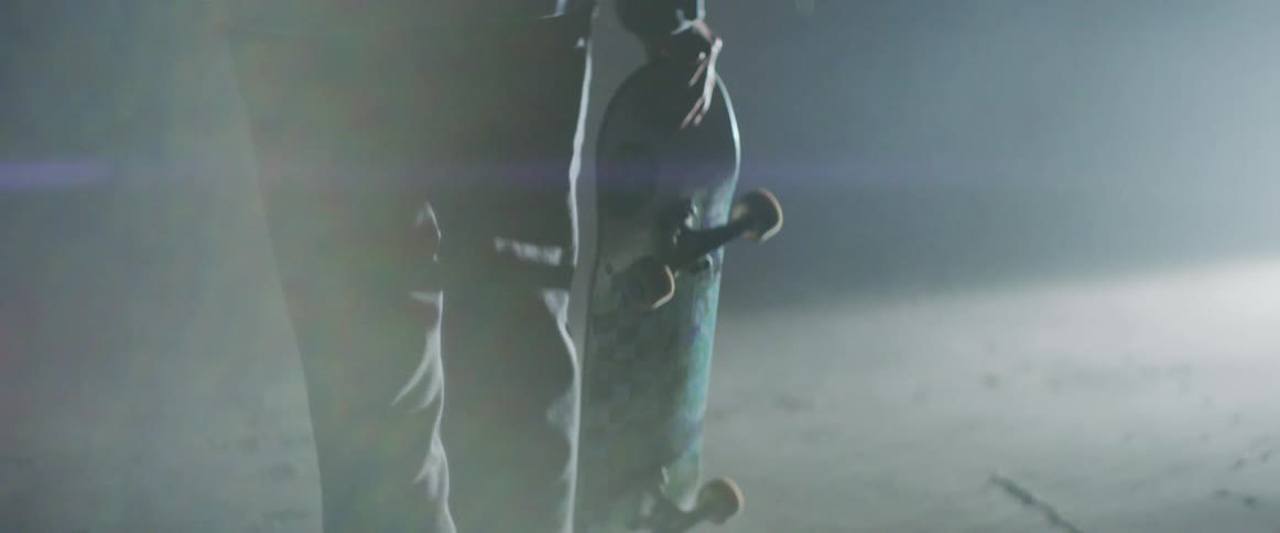 Skateboarder carries skateboard while paralleling red laser line in shadowed room lit by bright light