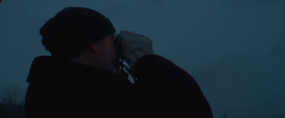 A man stands outside in the evening and takes a picture with a camera