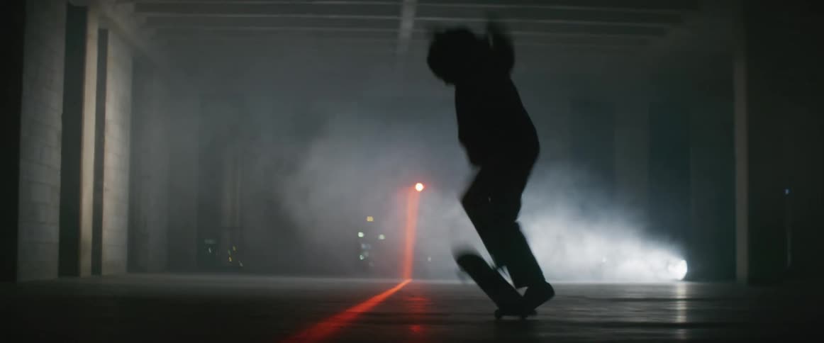 A man rides a skateboard through a smoke filled parking garage