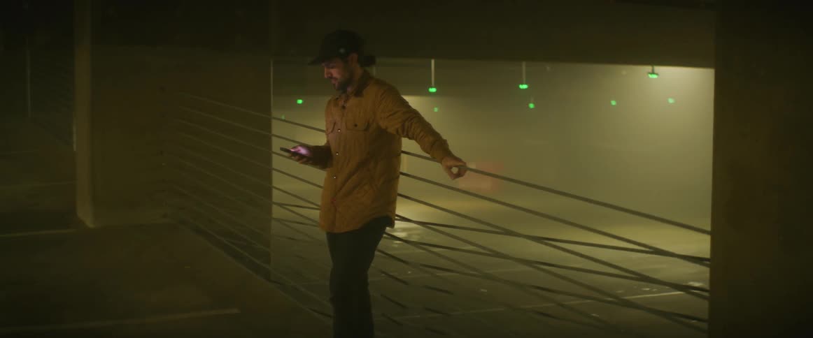 A man uses his smartphone while leaning against the railing in a parking garage