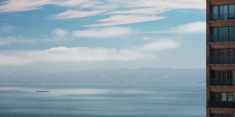 Apartment stands need water as ship cuts through channel paralleling foggy shore