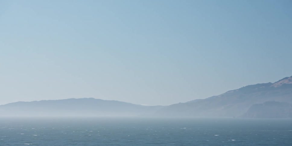 A layer of ice covers the ocean near a mountain range