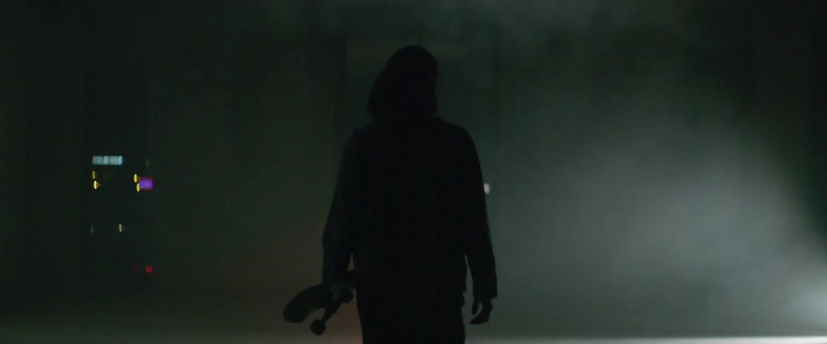 Skateboarder walks through fog toward wall opening showing city