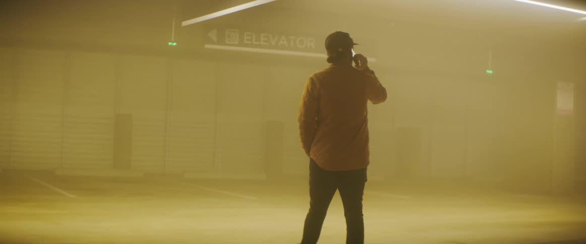 Man wearing a baseball hat and a jacket uses a smartphone inside a foggy parking garage