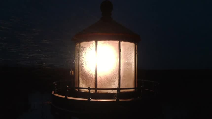 Rotating beacon in lighthouse outlines flurry during storm at night