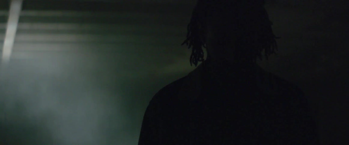 Silhouette of a man walking in a dark smoke filled room with candles burning behind him