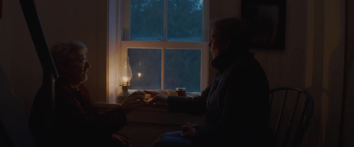 Old man and woman sitting next to a window and eating appetizers while talking to each other