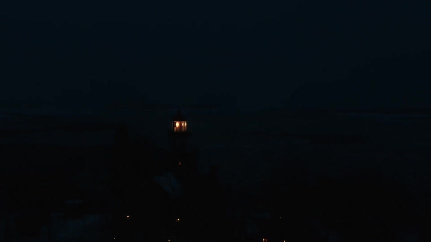 Beacon rotates in top of lighthouse set on shore at night