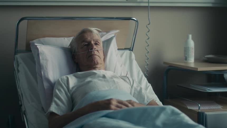 An elderly man appears frail as he lays in a hospital bed