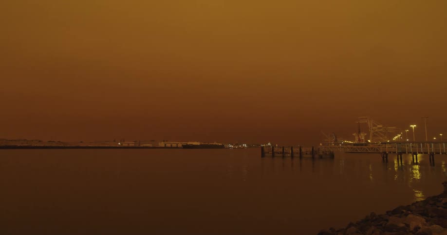 Water reflects waterfront lights under a red sky
