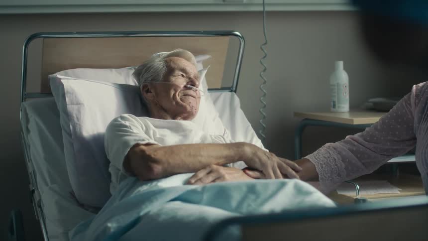 An elderly man is comforted as he lays in a hospital bed