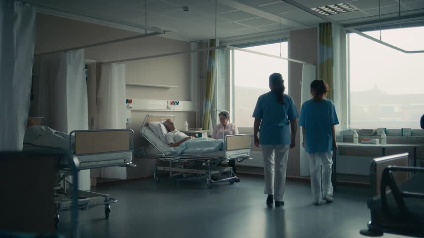 Nurses walk into a hospital room to chat with a patient and his wife