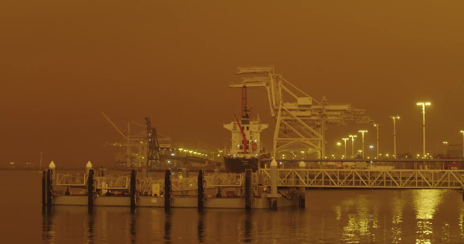 A ship docked near cargo cranes with light shimmering on the water surface at night