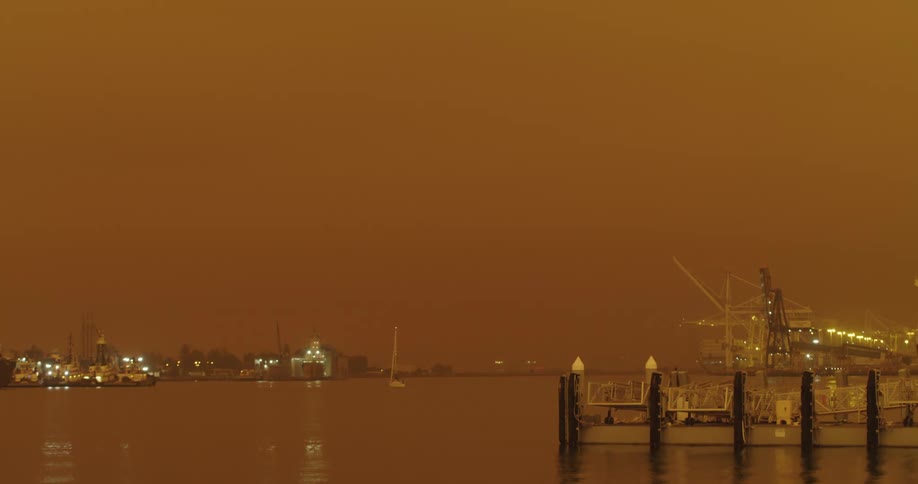 A waterfront harbor containing boats is seen beneath an ominous orange sky
