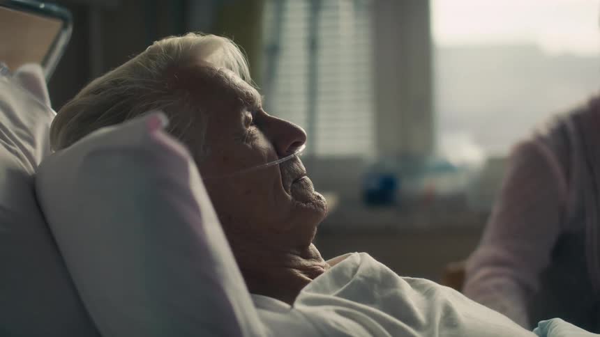 Elderly hospital patient listens and talks while his wife sits nearby