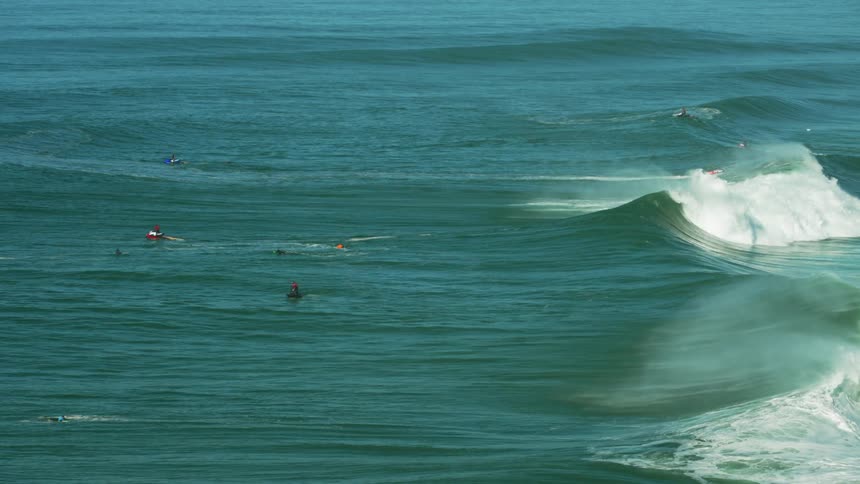 People surfing and riding their jet skis at the ocean while big waves are reaching the coast