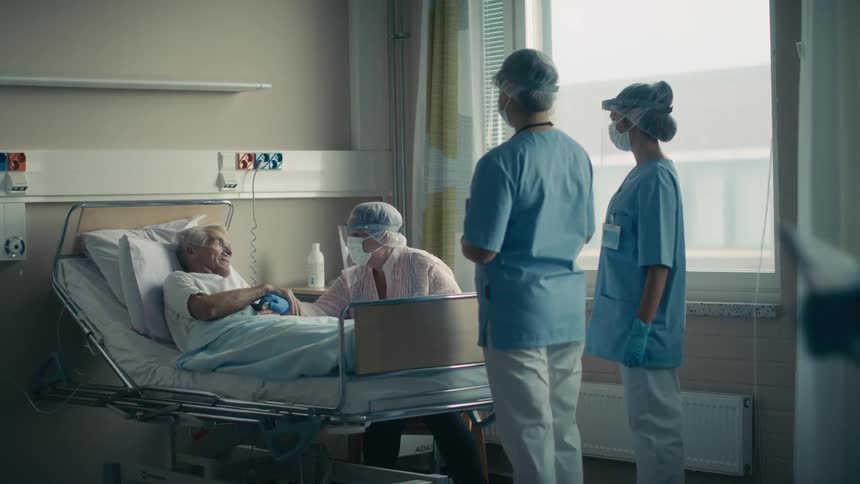 Nurses in masks with a face shield talk to patient and a visitor also wearing a face mask