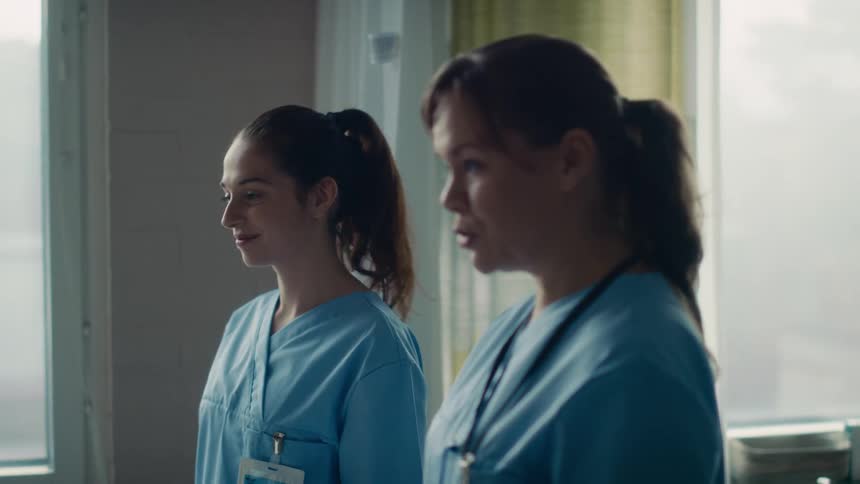 Doctor and nurse both wear scrubs as they talk to person while standing in hospital room