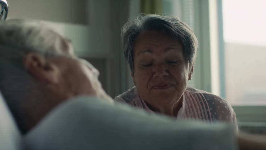 Wife sits next to husbands hospital bed as they get news from doctor