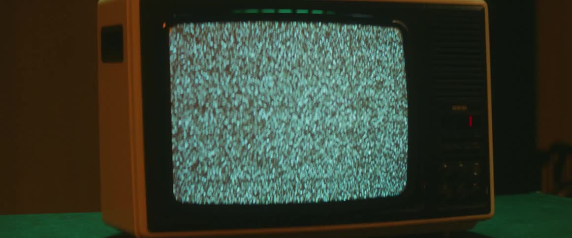Static and white noise on the screen of a vintage television over a table inside a room