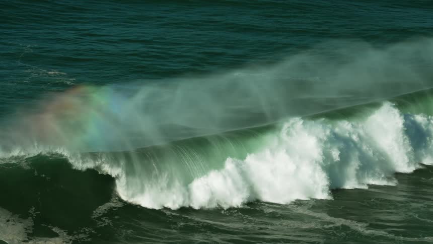 A rainbow is seen in the spray over a large wave making a perfect barrel as it crashes over