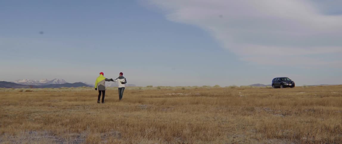 Two People Walk Toward Each Other Across a Grass Field With Warm Smiles and Ease.