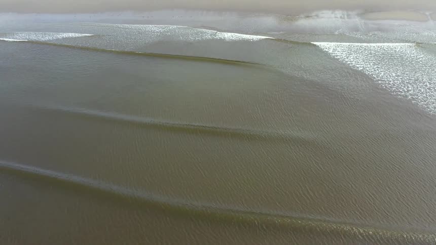 Ocean waves wash into a sandy beach during the day