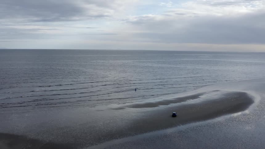 Person stands just off beach among waves on cloudy day