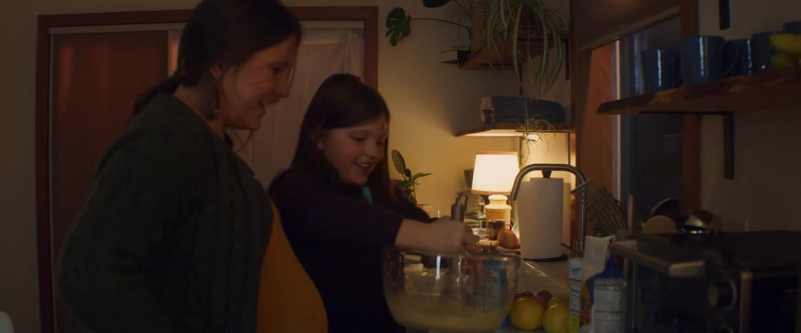 A mother and daughter mix cooking ingredients together in a glass mixing bowl in a home kitchen