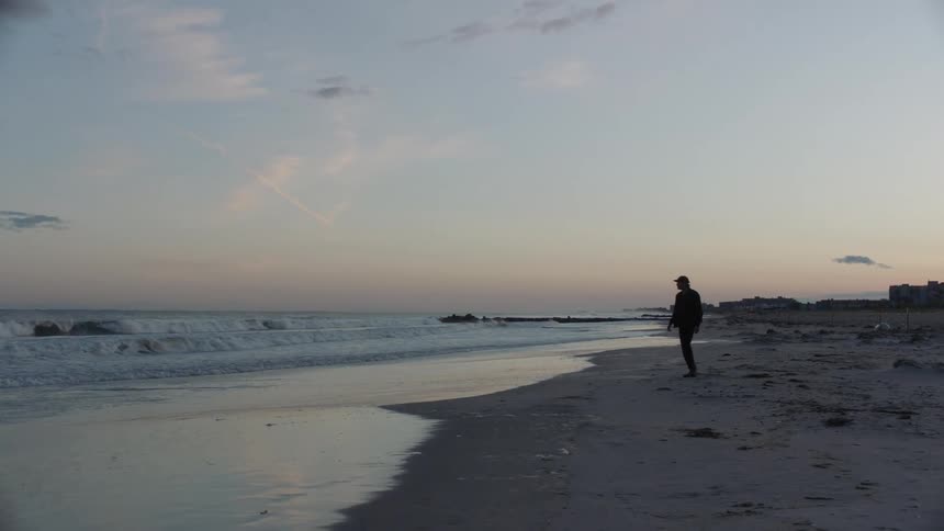 Man walking alone at the beach next to the ocean during sunset