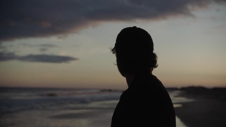 White man standing at the beach and looking around during sunset next to the ocean