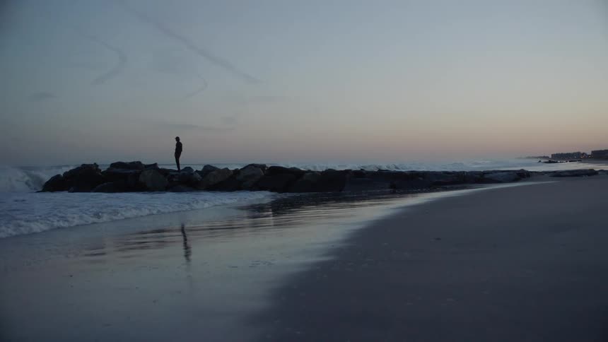 Silhouette of a man standing over a breakwater on the coast near the beach at sunset