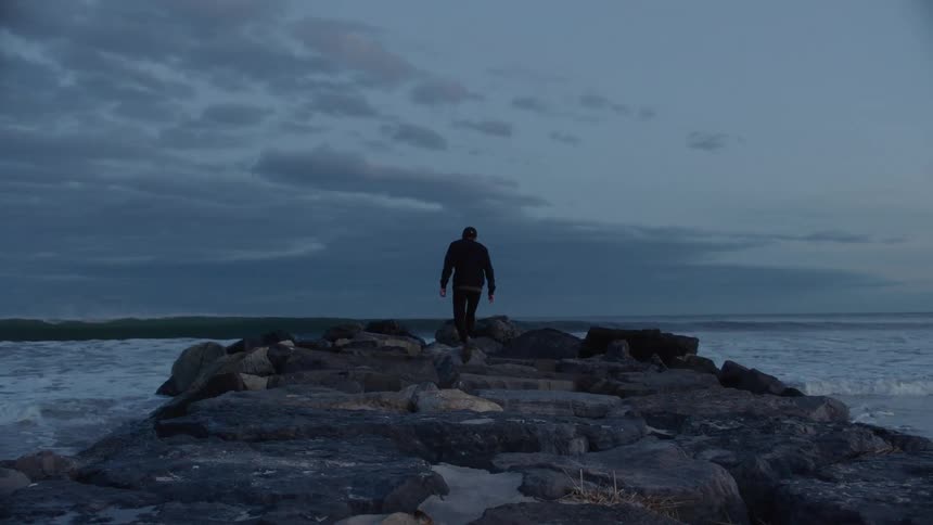 Man walking towards the ocean on some rocks