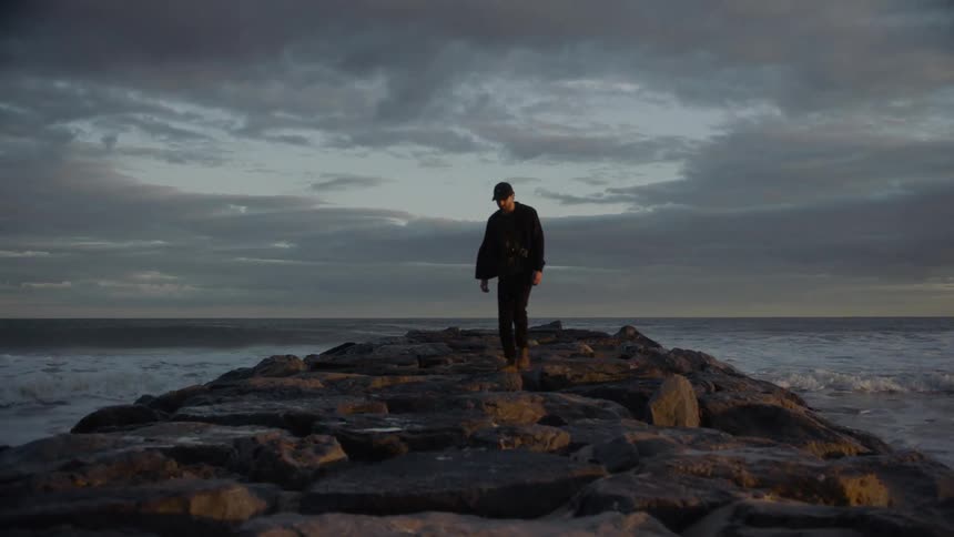 A man is walking on a rocky beach near choppy waves
