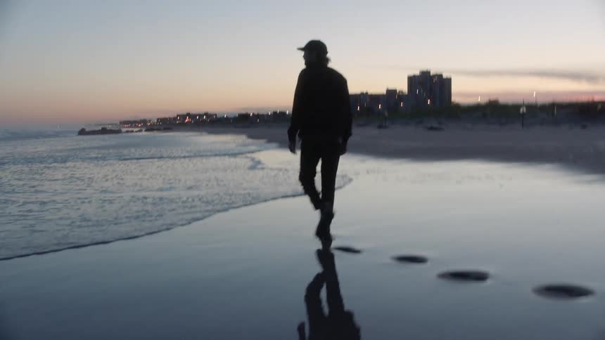 A man walks across the wet sand beach towards the water