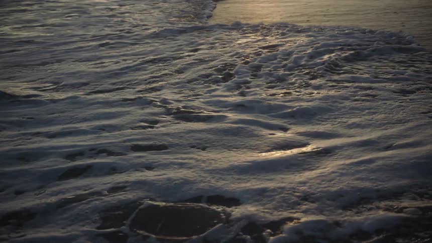 Gentle ocean waves wasing over the sand of a beach at sunset