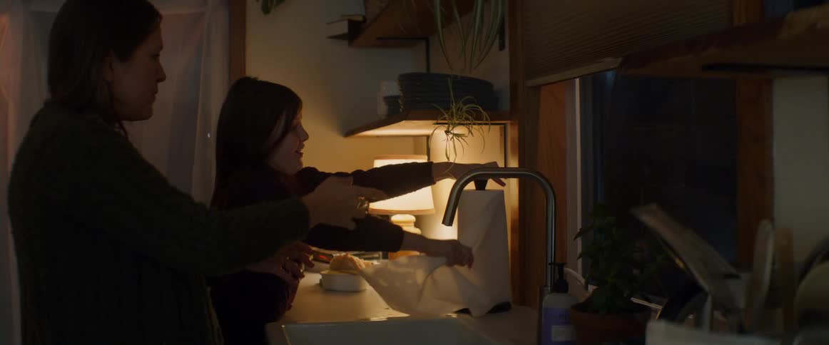 Pregnant mother and daughter dry their hands with paper towel in the kitchen at night