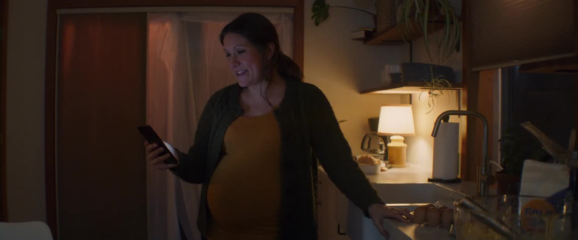 Woman stands near sink video calling and showing her pregnant belly
